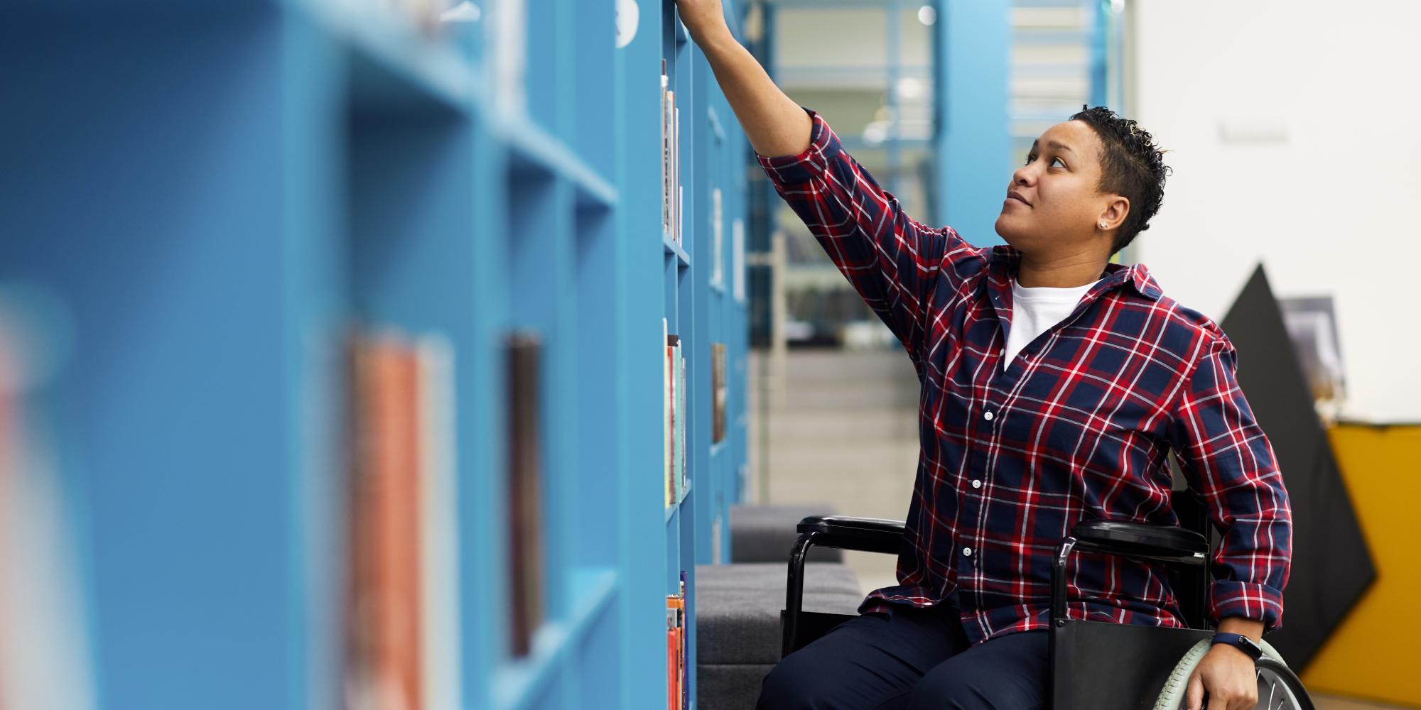 Student in wheelchair browses shelves in library