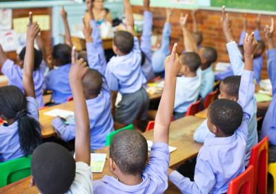 image of children in a classroom raising hands